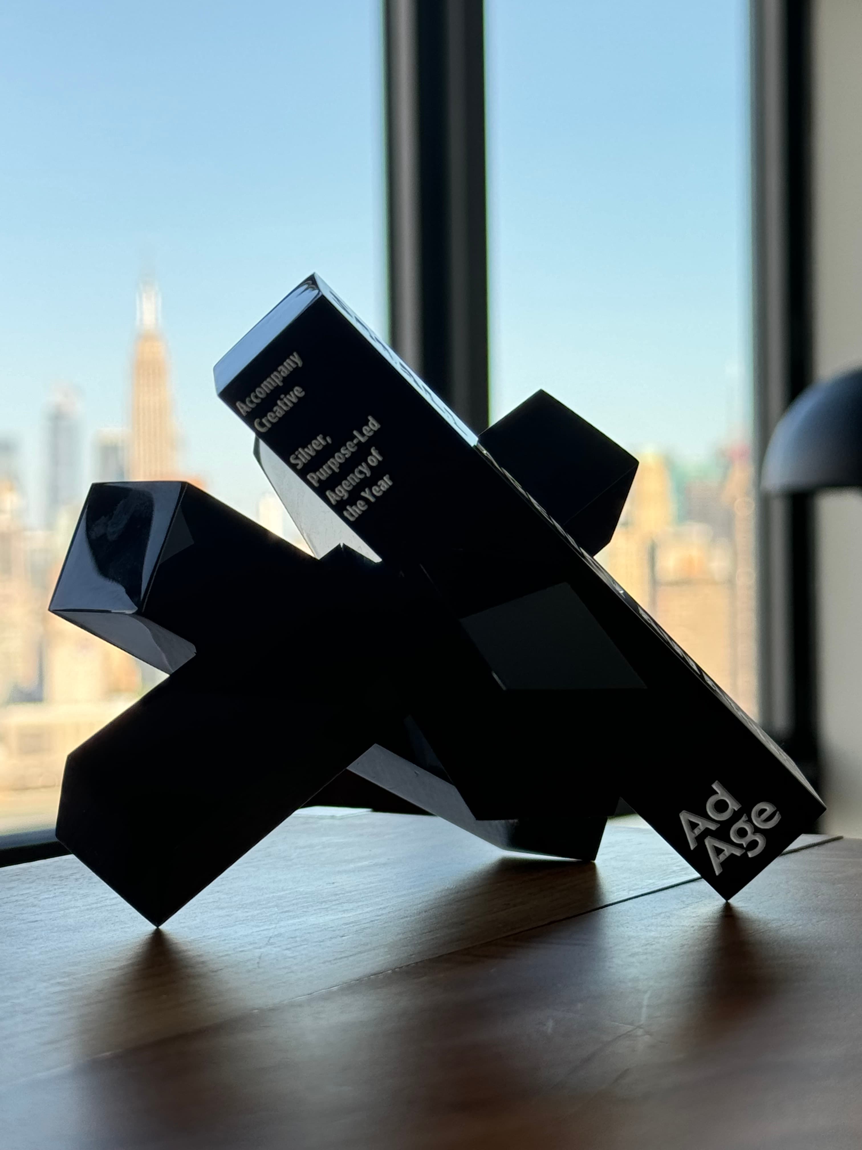 A black geometric Ad Age trophy on a wooden desk, engraved Accompany Creative Silver, Purpose-Led Agency of the Year