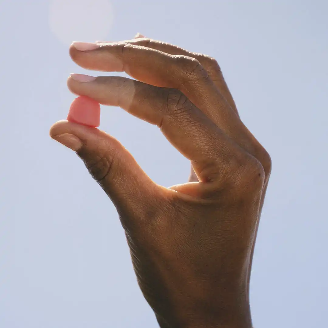 A brown-skinned hand pinches a pink gummy supplement against a blue sky for Nature's Bounty