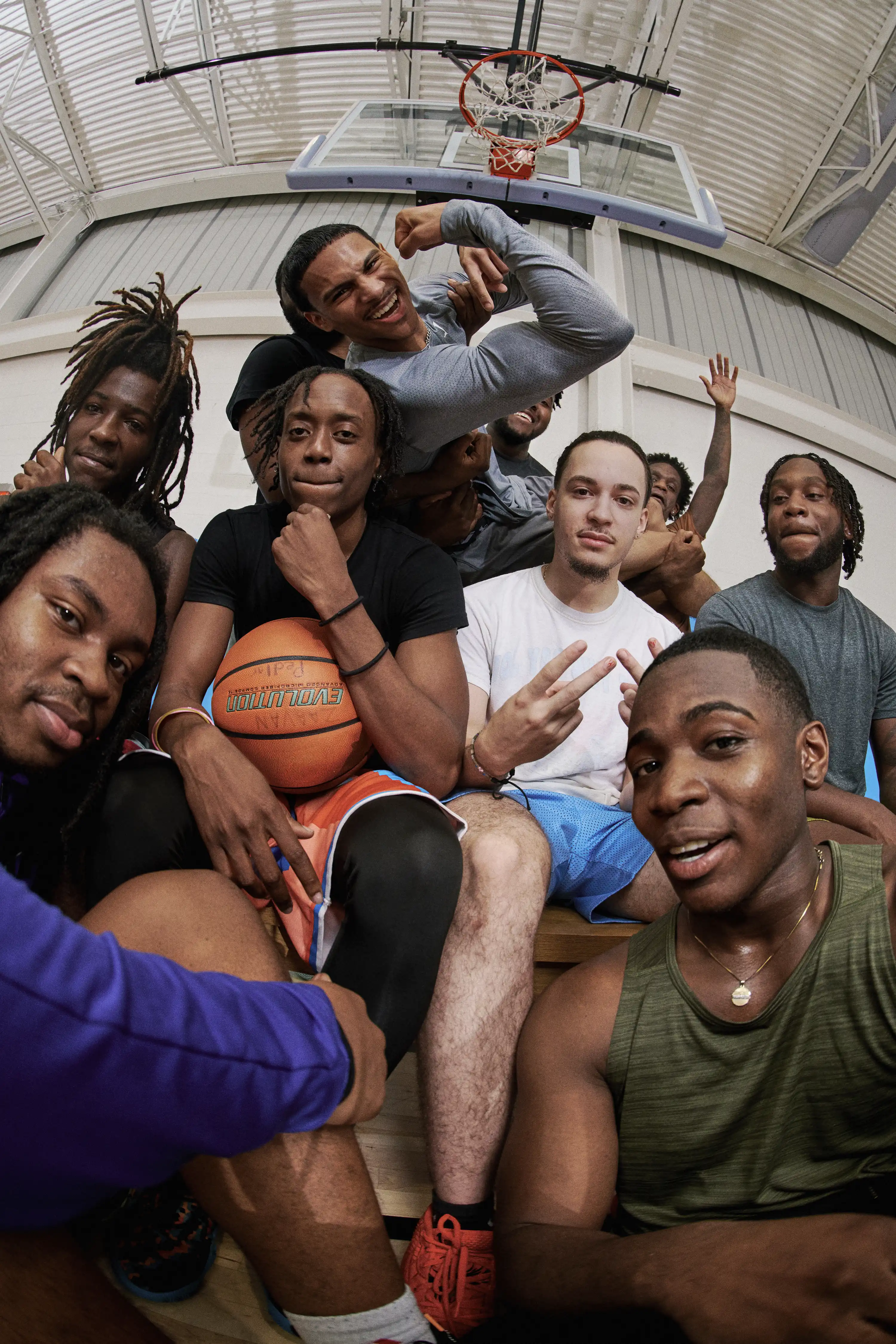 Young men crowd a gym bench under a basketball hoop, one holding a ball, fisheye selfie for the YMCA