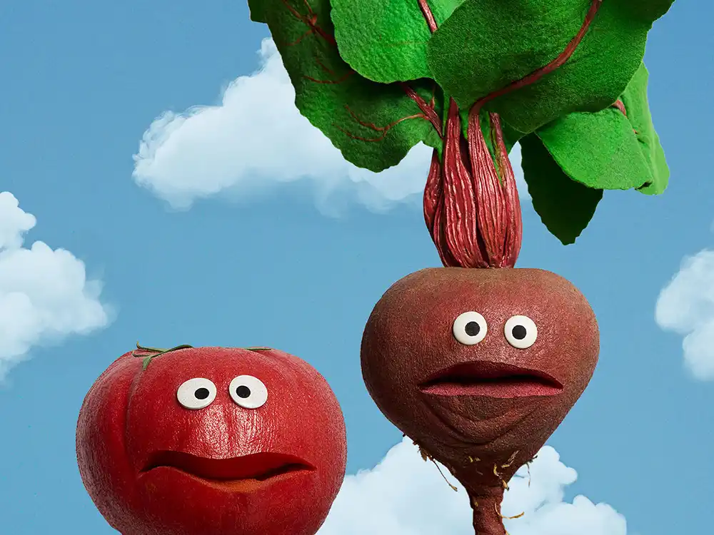 A tomato puppet and a beet puppet with leafy tops stand against a blue sky, from Compleat x Elmo's What Is Better Than How