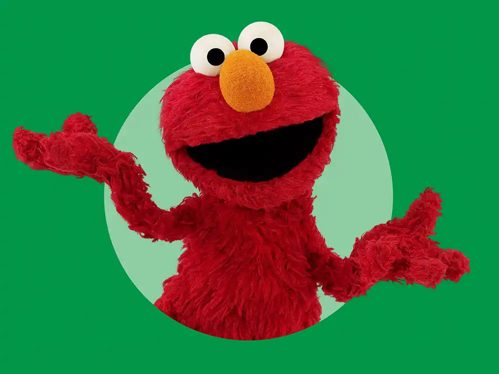Elmo shrugs with both arms open against a green circle, from Compleat x Elmo's What Is Better Than How