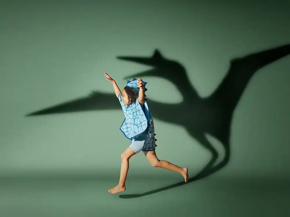 Child in a blue dinosaur hooded towel runs with a pterodactyl shadow, from Jurassic World's Preserving Legacies of the Past collection