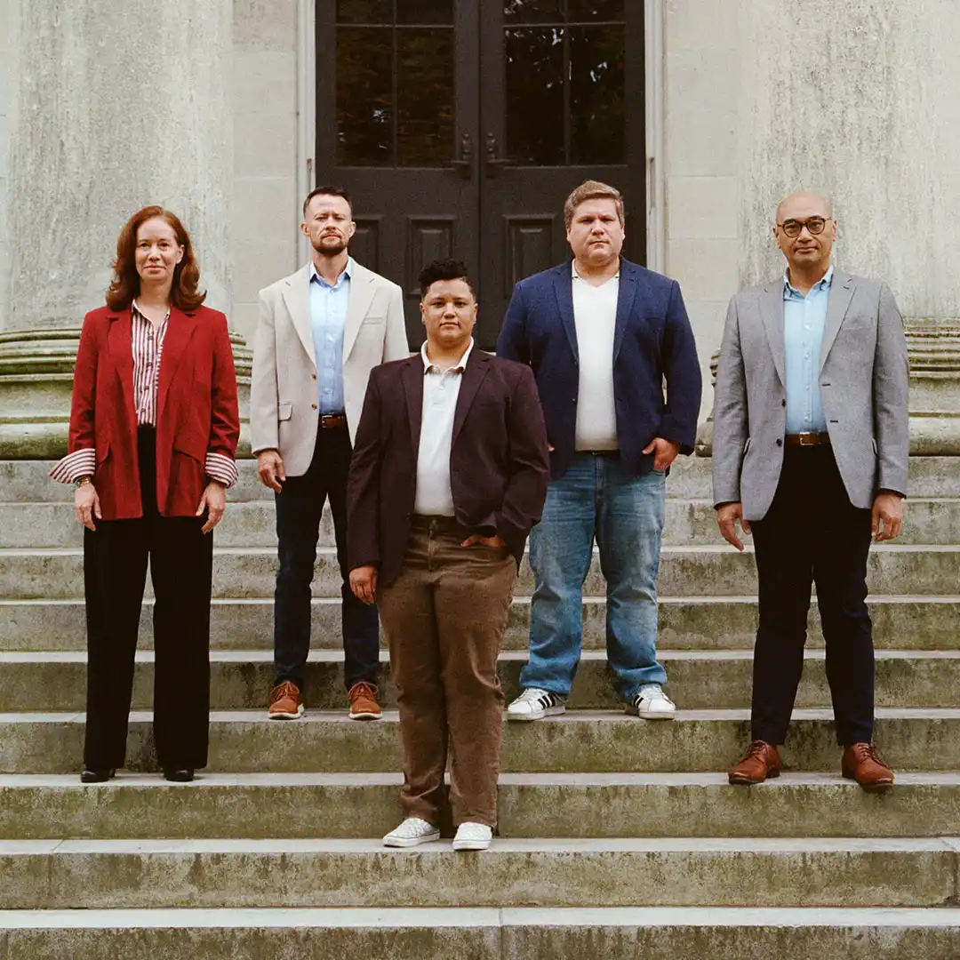 Five people in blazers stand on stone courthouse steps facing the camera