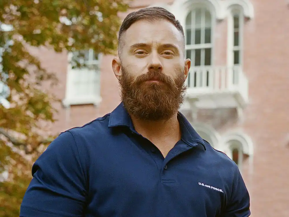Bearded man in a navy U.S. Air Force polo stands before a brick building, from Lambda Legal's All Rise campaign