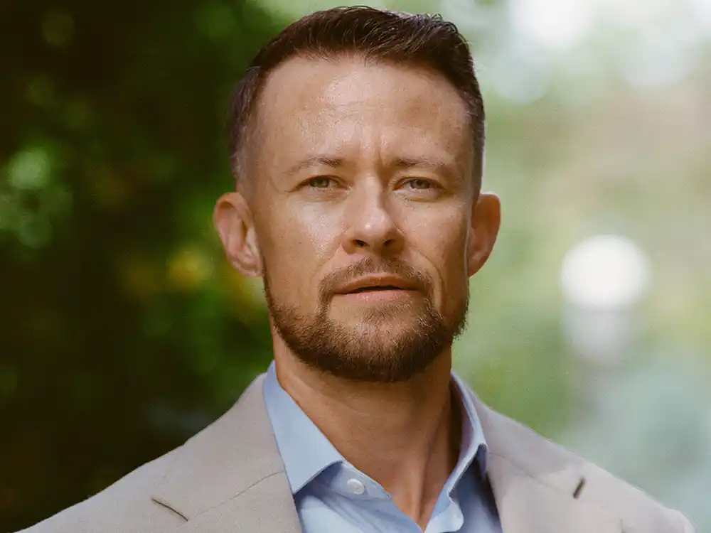 Close-up of a man with a short beard in a beige blazer and blue shirt, from Lambda Legal's All Rise campaign