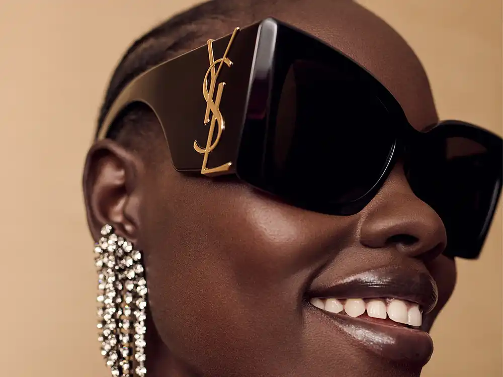 Woman smiles in oversized black YSL sunglasses and a crystal chandelier earring, from Vestiaire Collective's Parlez-vous?