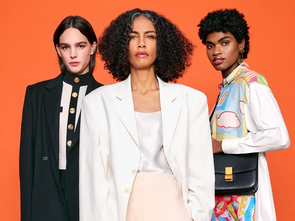 Three women in mixed luxury looks stand against orange, from Vestiaire Collective's Parlez-vous?