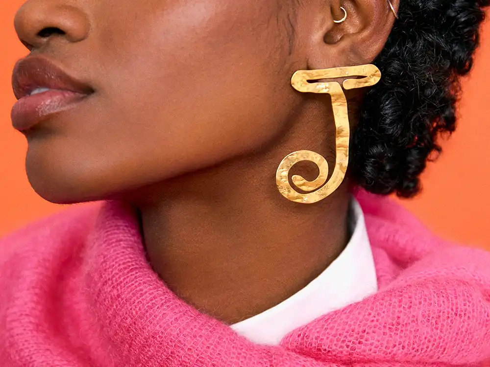 Close-up of a hammered gold J earring against a bright pink knit, from Vestiaire Collective's Parlez-vous?
