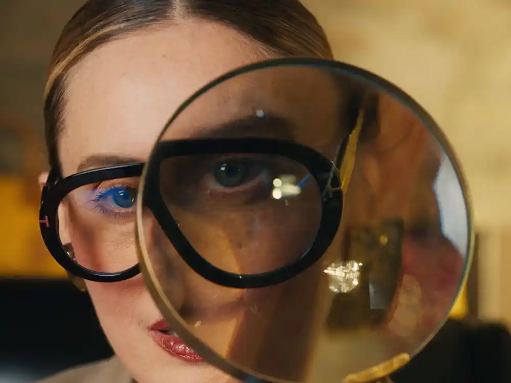 Close-up of a woman in black glasses, one eye magnified through a round lens, from Vestiaire Collective's Parlez-vous?