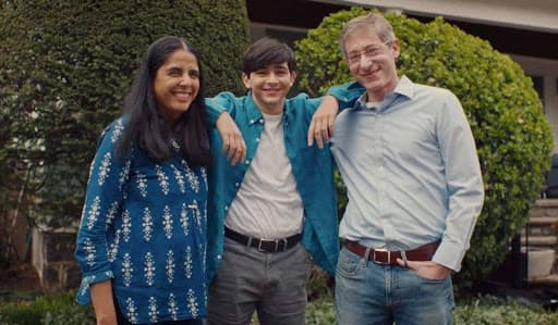 Avni, Sonu, and Josh Gupta-Kagan stand together smiling outside in a family portrait