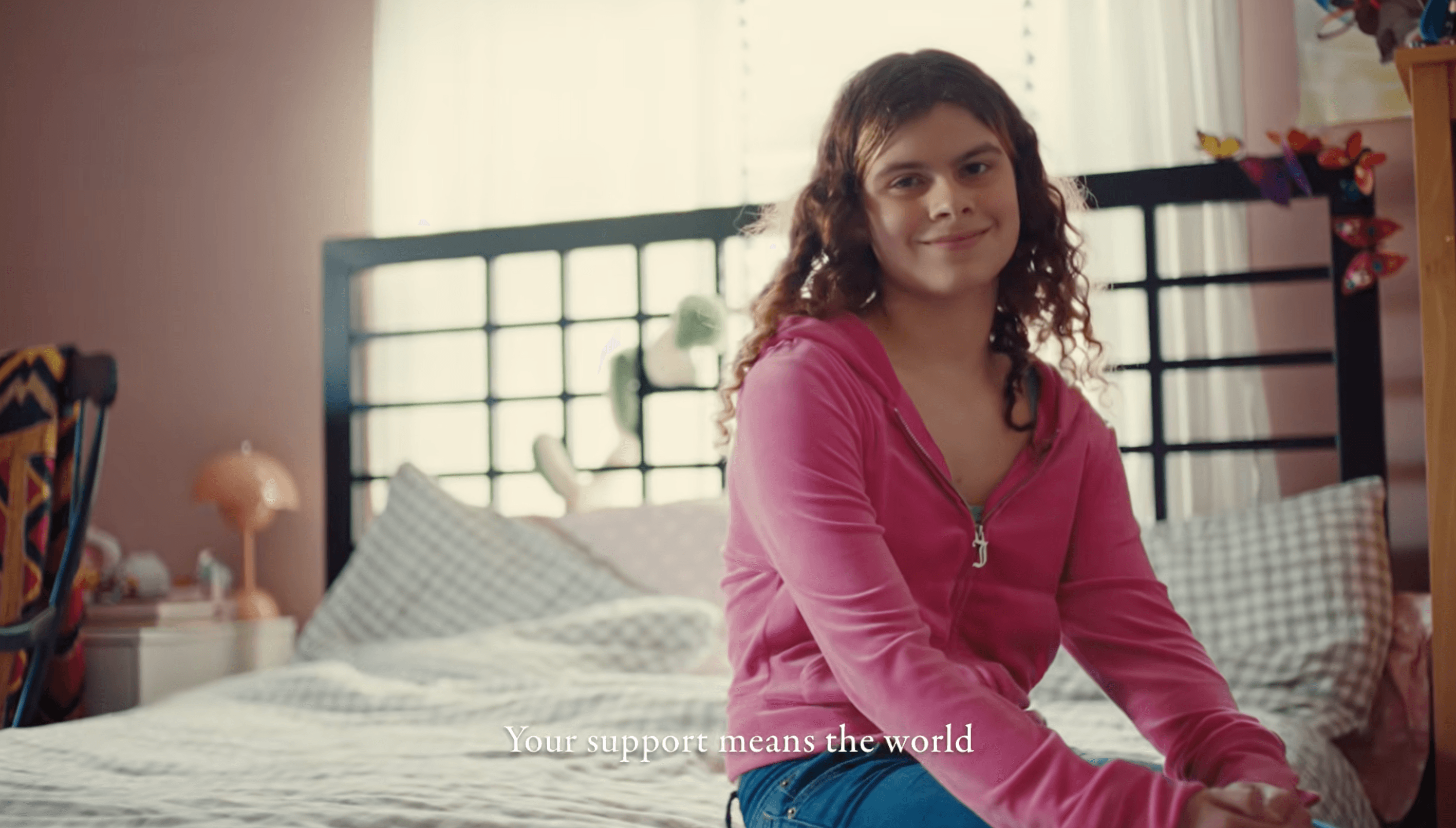Emma, a trans teenager, sits on her bed smiling, with the caption 'Your support means the world'
